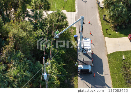 Maintenance of electrical grid by city utility cervices. Worker in lift truck trimming tree around power lines 137008453