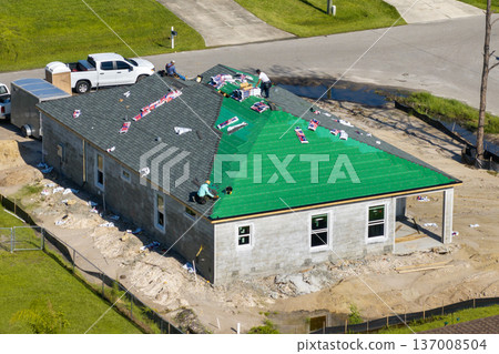 Construction workers building house rooftop with asphalt shingles. Real estate housing development. 137008504