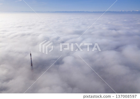 Aerial top view of foggy cloudy landscape with radio or TV antenna top on blue sky copy space background and mountain ridge on horizon. Aerial top view of foggy cloudy landscape with radio or TV antenna top on blue sky copy space background and mountain ridge on horizon. 137008597