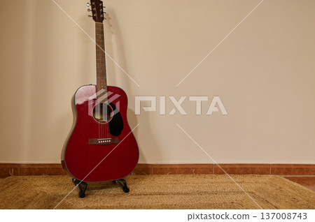 Red Acoustic Guitar Leaning Against Wall on Woven Rug in Minimal Interior Red Acoustic Guitar Leaning Against Wall on Woven Rug in Minimal Interior 137008743