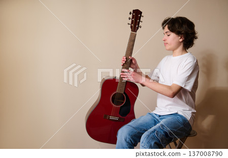 Teen Boy Holding Red Acoustic Guitar While Sitting On Stool Practicing Music Teen Boy Holding Red Acoustic Guitar While Sitting On Stool Practicing Music 137008790