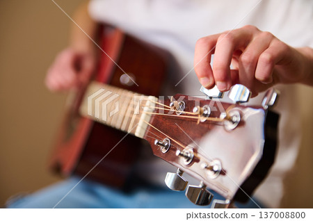 Close-Up Of Hand Tuning Acoustic Guitar Strings On Wooden Headstock 137008800