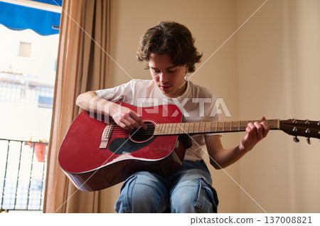Teen Boy Playing Red Acoustic Guitar Indoors Practicing Music At Home Teen Boy Playing Red Acoustic Guitar Indoors Practicing Music At Home 137008821