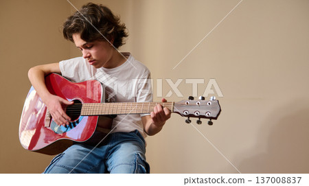 Teen Boy Playing Red Acoustic Guitar Seated Indoors Practicing Music Teen Boy Playing Red Acoustic Guitar Seated Indoors Practicing Music 137008837