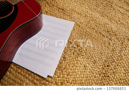 Red Acoustic Guitar Resting on Sheet Music on Woven Mat for Songwriting and Practice Red Acoustic Guitar Resting on Sheet Music on Woven Mat for Songwriting and Practice 137008851