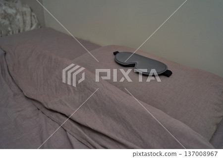 Gray sleep mask resting on neatly made bed with soft gray linens in calm bedroom setting 137008967