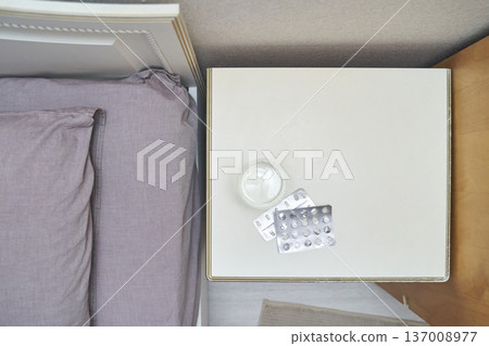 Top-down view of bedroom nightstand with empty pill blisters and water glass 137008977