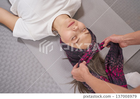 Young caucasian female relaxation during head massage with colorful scarf on yoga mat Young caucasian female relaxation during head massage with colorful scarf on yoga mat 137008979