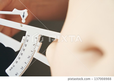 Close-up of body fat caliper measuring young caucasian females skin for fitness assessment 137008988