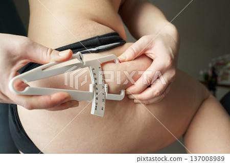 Female adult checking body fat percentage with caliper on thigh for fitness and health evaluation 137008989