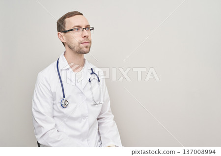 Caucasian male doctor in white coat with stethoscope looking confidently to the side Caucasian male doctor in white coat with stethoscope looking confidently to the side 137008994