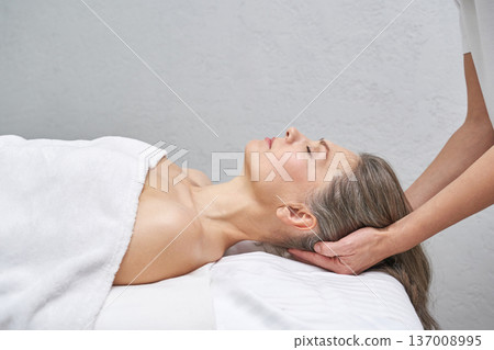 Mature caucasian woman relaxing during head massage therapy session in a spa setting for stress Mature caucasian woman relaxing during head massage therapy session in a spa setting for stress 137008995