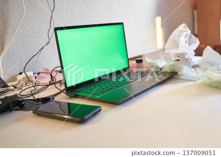 Laptop And Smartphone With Green Screens On Cluttered Desk In Modern Workspace Environment Laptop And Smartphone With Green Screens On Cluttered Desk In Modern Workspace Environment 137009051