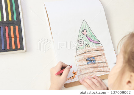 Young caucasian female child drawing colorful house with crayons on white paper Young caucasian female child drawing colorful house with crayons on white paper 137009062