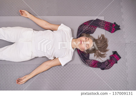 Relaxed mature caucasian woman meditating in yoga pose on yoga mat indoors with scarf Relaxed mature caucasian woman meditating in yoga pose on yoga mat indoors with scarf 137009131
