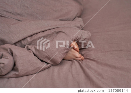 Cozy childs feet under pink blanket on bed reflecting comfort, warmth, and relaxation Cozy childs feet under pink blanket on bed reflecting comfort, warmth, and relaxation 137009144