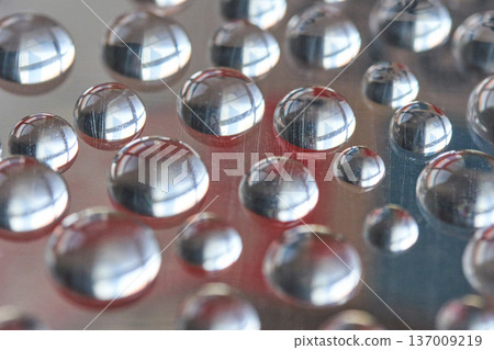 Close-up of reflective water droplets on smooth surface capturing light and colorful abstract 137009219