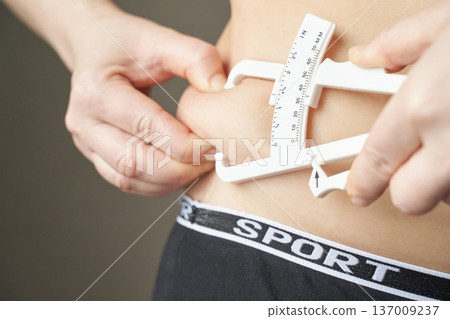 Female measuring body fat percentage with caliper tool on stomach 137009237