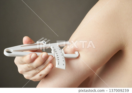 Female hands using skinfold caliper for body fat measurement on arm close-up Female hands using skinfold caliper for body fat measurement on arm close-up 137009239