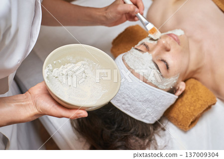 Female Caucasian Young Adult Receiving Facial Treatment With Clay Mask In Spa Setting Female Caucasian Young Adult Receiving Facial Treatment With Clay Mask In Spa Setting 137009304