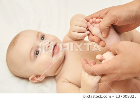 Caucasian Infant Smiling At Caregiver Holding Feet On Soft White Background Caucasian Infant Smiling At Caregiver Holding Feet On Soft White Background 137009323