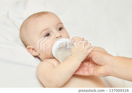 Caucasian Baby Drinking From Bottle Held By Adult Hand On White Background 137009326