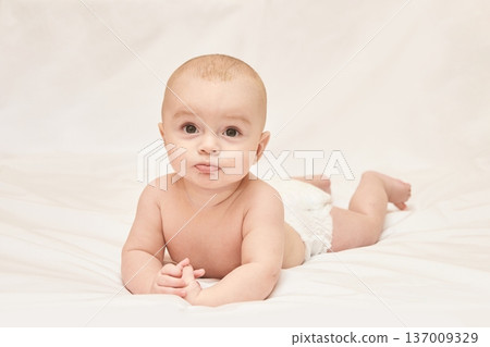 Cute Caucasian Baby Lying On White Sheets With Curious Expression In A Diaper 137009329