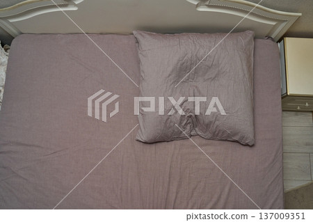 Empty bed with crumpled pillow and mauve sheets in minimalist bedroom setting Empty bed with crumpled pillow and mauve sheets in minimalist bedroom setting 137009351