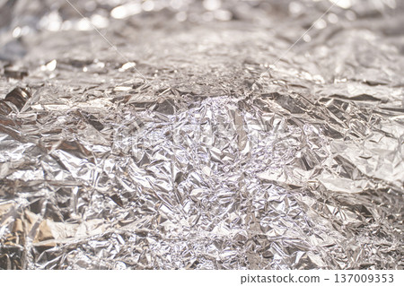 Crumpled silver aluminum foil texture with shiny reflective surface and abstract pattern 137009353