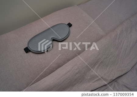 Gray sleep mask resting on pink linen sheets for relaxation and comfort in a serene bedroom setting 137009354