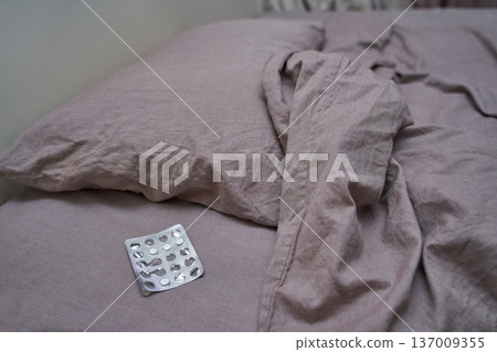 Unmade bed with empty blister pack on pink sheets depicting neglect and anxiety 137009355