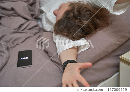 Young african female stretching in bed with smartphone alarm on brown linens 137009359
