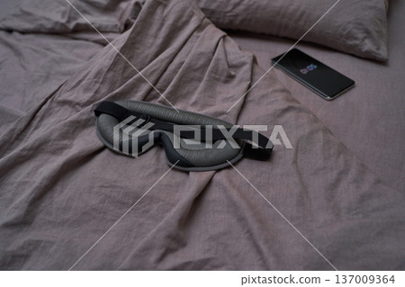 Sleep mask on bed with smartphone displaying alarm time for relaxation and restful sleep routine Sleep mask on bed with smartphone displaying alarm time for relaxation and restful sleep routine 137009364