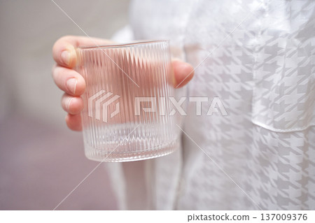 Caucasian female holding clear glass tumbler wearing white patterned shirt indoors elegance Caucasian female holding clear glass tumbler wearing white patterned shirt indoors elegance 137009376