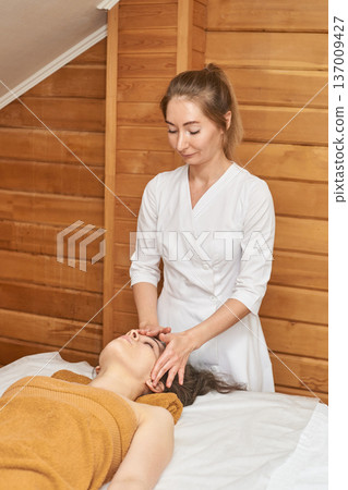 Female Therapist Performing Facial Massage On Young Caucasian Woman In Relaxing Spa Setting Female Therapist Performing Facial Massage On Young Caucasian Woman In Relaxing Spa Setting 137009427