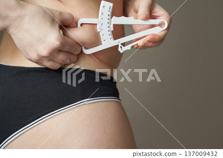 Young caucasian female measuring body fat with caliper in fitness and health concept image 137009432