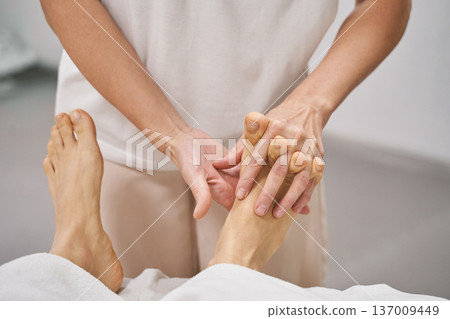 Female caucasian adult performing therapeutic foot massage in a relaxing wellness spa setting Female caucasian adult performing therapeutic foot massage in a relaxing wellness spa setting 137009449