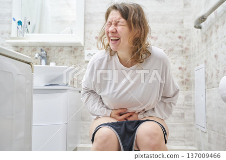 Caucasian female adult experiencing pain in bathroom setting, expressing discomfort and tension Caucasian female adult experiencing pain in bathroom setting, expressing discomfort and tension 137009466