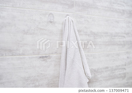 White towel hanging on rustic bathroom wall hook with soft earthy gray tones and textured tiles White towel hanging on rustic bathroom wall hook with soft earthy gray tones and textured tiles 137009471