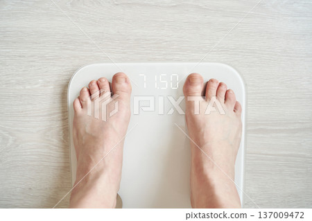 Caucasian adult feet on digital scale displaying weight on light wood floor for health and fitness Caucasian adult feet on digital scale displaying weight on light wood floor for health and fitness 137009472