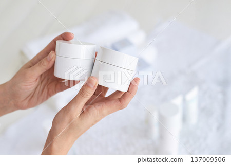 Hands holding skincare cream jars against soft focus background in spa setting Hands holding skincare cream jars against soft focus background in spa setting 137009506