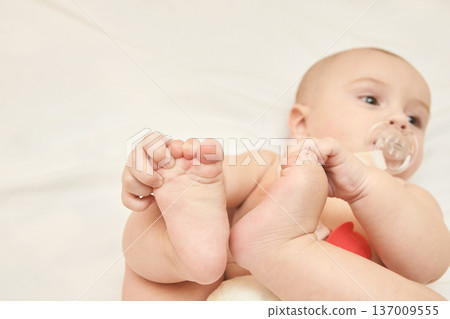 Caucasian Infant With Pacifier Lying On Bed Showing Feet, Expressing Innocence And Playfulness 137009555