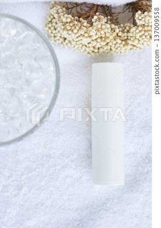 Minimalist skincare setup with white bottle on soft towel surrounded by flowers and glass beads Minimalist skincare setup with white bottle on soft towel surrounded by flowers and glass beads 137009558