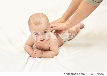 Caucasian Baby Lying On White Sheet With Adult Hands Providing Gentle Care In Bright Room Setting 137009587