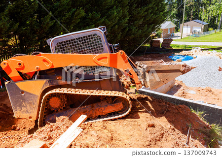 Small excavator bucket moves dirt, gravel while workers prepare construction site for building. Small excavator bucket moves dirt, gravel while workers prepare construction site for building. 137009743