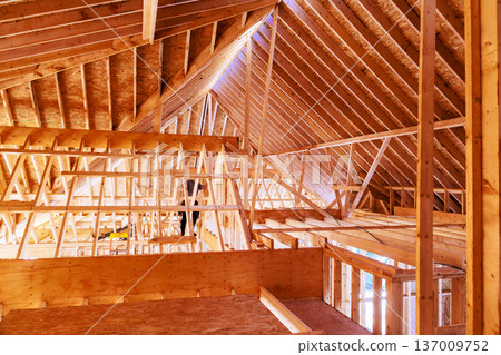 Construction site features wooden framework with beams trusses forming an open attic space in new house. 137009752
