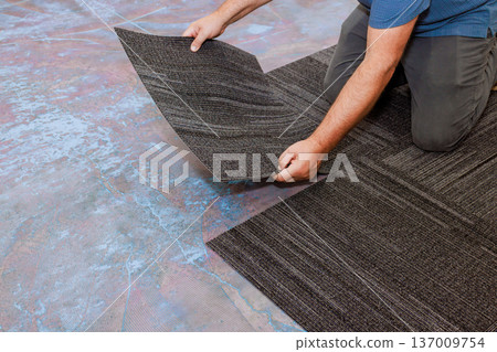 Man on his knees places carpet tiles on colorful floor, ensuring they fit snugly together Man on his knees places carpet tiles on colorful floor, ensuring they fit snugly together 137009754