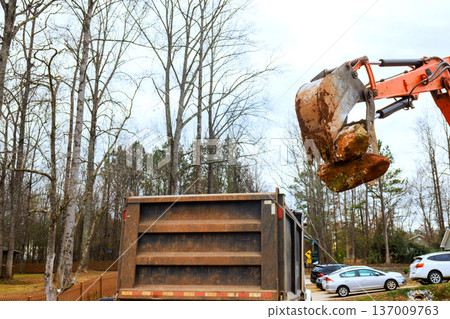 Workers use backhoe to load dirt rocks into dump truck at residential site Workers use backhoe to load dirt rocks into dump truck at residential site 137009763