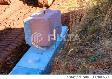 Large concrete block is being lifted by equipment at construction site to place it on retaining walls 137009774