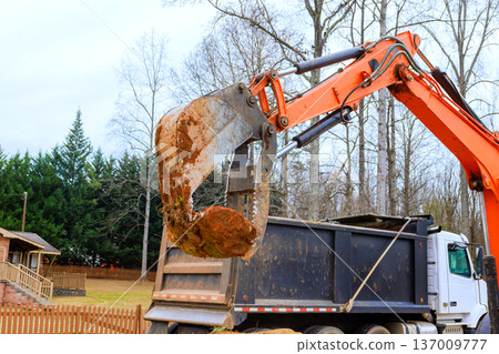 Heavy excavator lifts rocks from ground transfers it into truck during construction work process. Heavy excavator lifts rocks from ground transfers it into truck during construction work process. 137009777